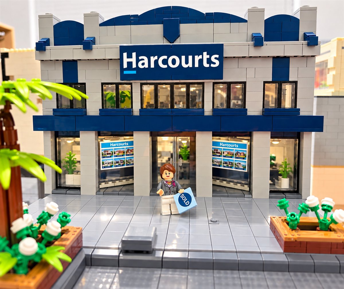 A LEGO model of the Harcourts office with a minifigure holding a SOLD sign